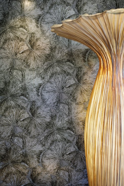 Wand mit organischem grauem Muster aus Argoprint, davor eine blumenartige Holzlampe