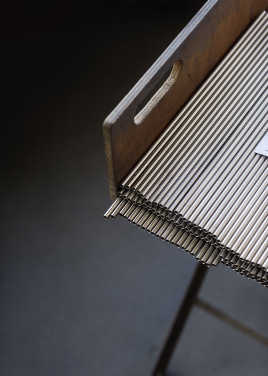 Diagonal abgeschnittene Ecke von einer Reihe von silbernen Metallröhrchen, die auf einem Holzgestell liegen.