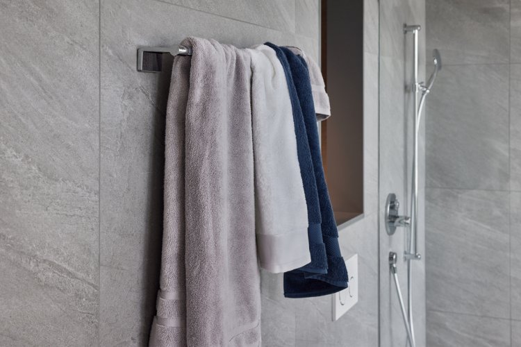 Silberne Badetuchstange an einer grauen Fliesenwand im Bad mit mehreren, zusammengedrängten Duschtüchern.