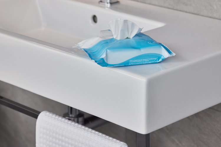 Blaue Packung mit Feuchttüchern steht auf der Ecke eines weissen Porzellanwaschbecken.