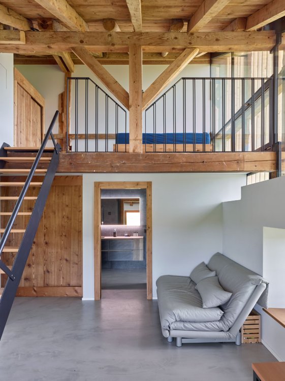 Holzgalerie in einem umgebauten Bauernhaus mit Treppe links, darunter eine Tür und ein graues Sofa