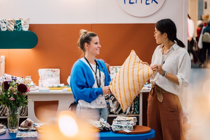 Zwei junge Frauen diskutieren über ein gestreiftes Kissen an einem Textilstand an den O-DAYS