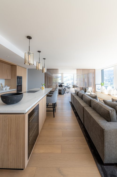 Lichtdurchflutete moderne Wohnung mit Küche aus Holz links und grauem Sofa rechts