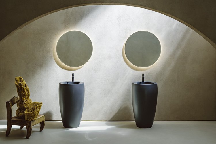 Zwei schwarze Waschtische mit runden Spiegeln in von oben beleuchtetem bogenförmigen Raum aus Beton