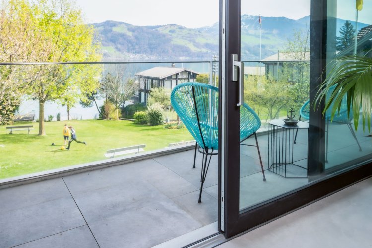 Halb offene Balkon-Schiebetür mit Gartenstühlen und Aussicht zum See