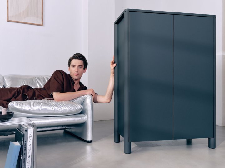 Mann auf Sofa neben dunklem Highboard