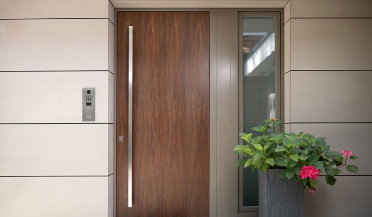 Haustür aus Holz mit DoorBird Schliessystem links und Blumentopf rechts