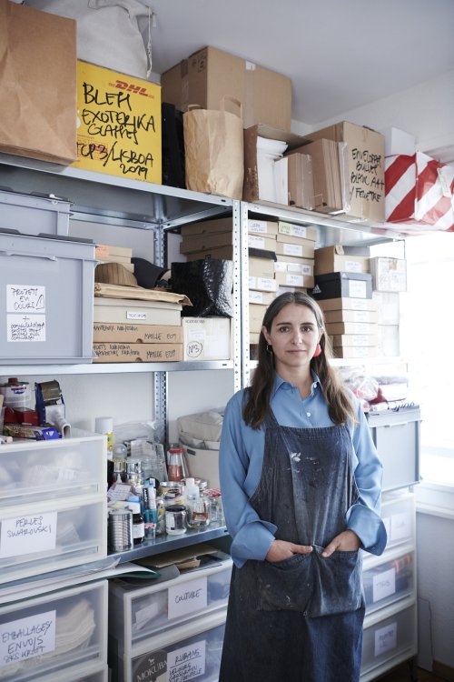 Ligia Dias vor einer Wand voll Schachteln mit den Händen in den Taschen ihrer dunklen Arbeitsschürze