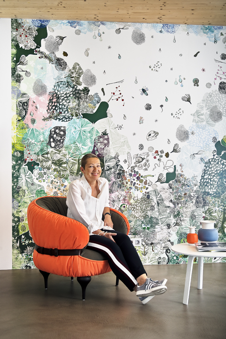 Katja Fahrenholz in einem orangen Sessel vor der Tapete «Grüss Gott» der Künstlerin Sara Ginola