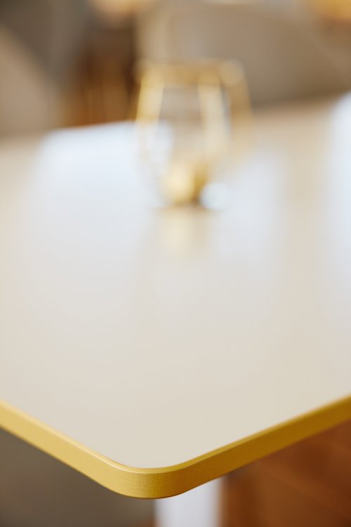 Ecke einer weissen Tischplatte aus einer HPL-Platte mit heller Holzoptik im Profil.
