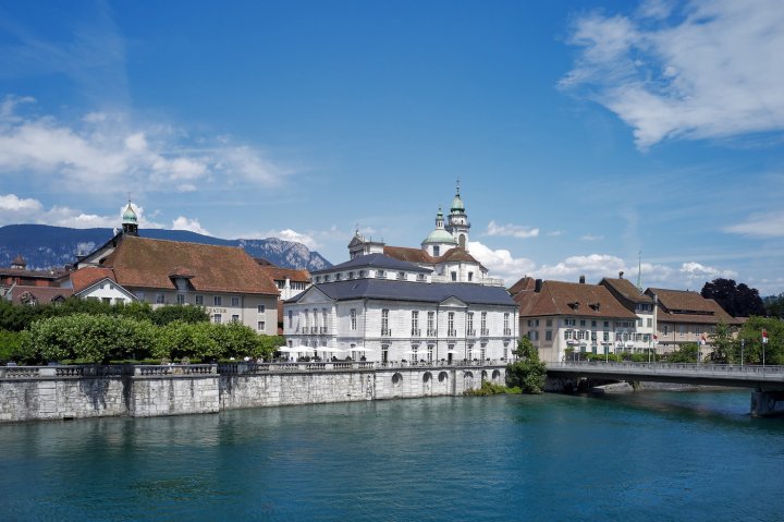 Blick über die Aare zum barocken Palais Besenval in Solothurn an einem sonnigen Tag mit blauem Himmel.