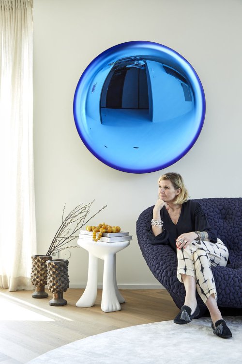 Gestalterin Carolin Stephan sitzt auf einem dunkelblauen Sofa rechts im Bild, daneben ein weisser Beistelltisch und an der Wand hinten ein glänzender, blauer Kreis.