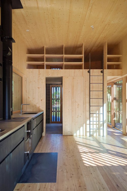 Blick aus Wohnküche an Holztrennwand zum Schlafzimmer mit oben integrierten Regalen.