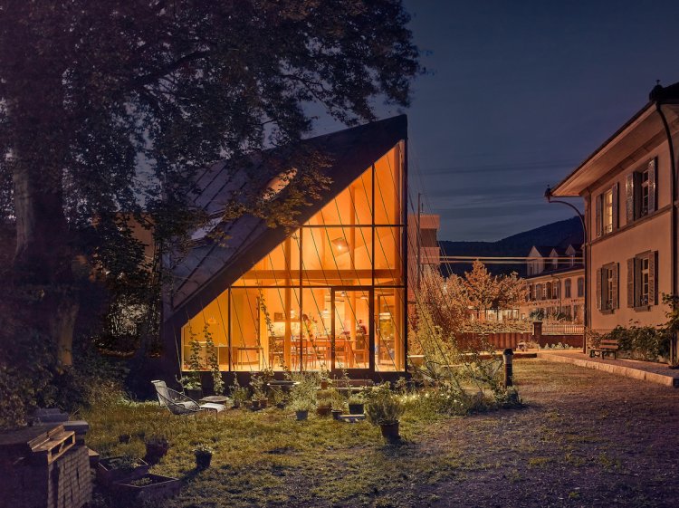 Ein zeltartiges Gebäude bei Nacht, von Innen beleuchtet, steht links neben einem historischen Herrschaftshaus