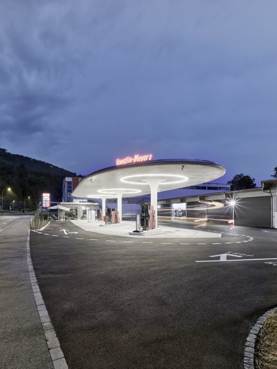Tankstelle in der nacht mit roter Leuchtanzeige auf dem Dach und beleuchteten Pilzsstützen