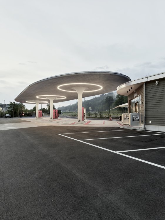 Tankstelle mit Betondach auf drei Pilzstützen, davor einige weiss eingezeichnete Parkplätze