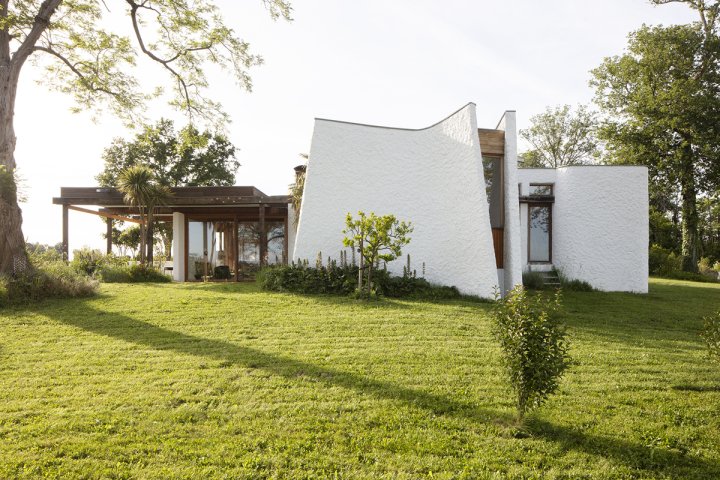 Aussenaufnahme eines futuristischen Hauses von Architekt Hans Demarmels aus den 1960er-Jahren auf einer grünen Wiese in Südwestfrankreich. Die Fassade besteht teils aus rauem Putz, teils aus Holz.