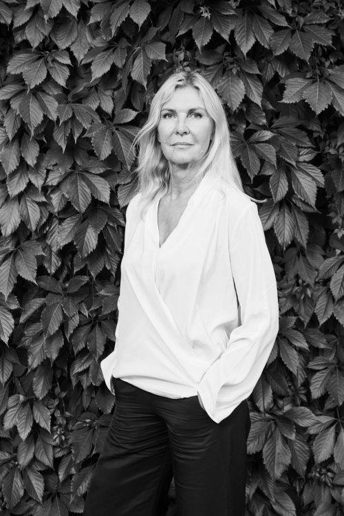 Schwarz-weiss Porträt der dänischen Architektin Dorte Mandrup. Sie steht vor einer Wand aus dichtem Efeu, trägt eine helle Bluse und blickt mit ruhigem, direktem Ausdruck in die Kamera.