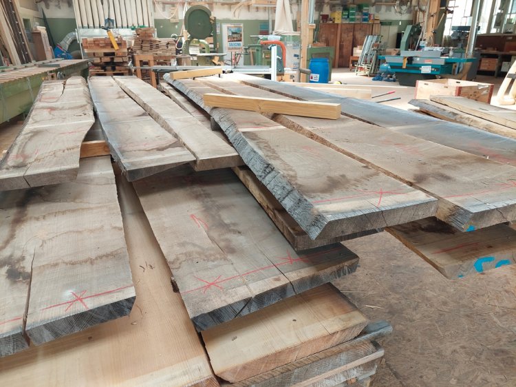 Stapel grob zugesägter Eschenbohlen mit roten Markierungen in einer Schreinerwerkstatt. Die rohen Holzbretter liegen bereit für die Weiterverarbeitung zum Pavillon-Fachwerk.