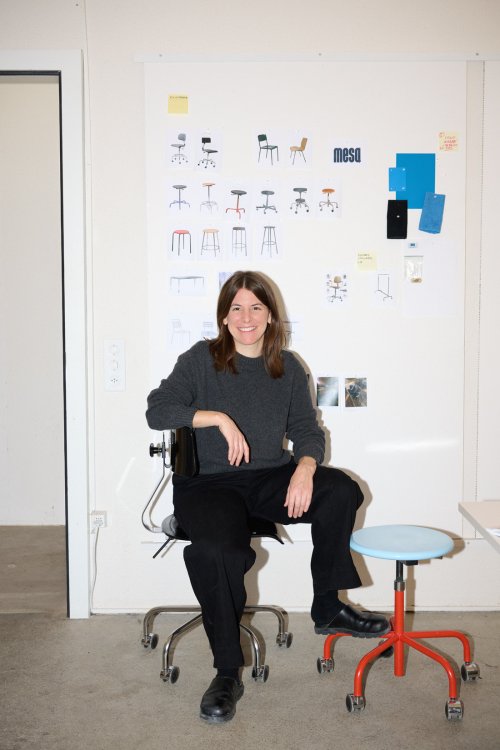 Porträt der Designerin Flavia Brändle im Atelier, sitzend vor einer Pinnwand mit Produktentwürfen, Stuhl-Skizzen und Farbproben.