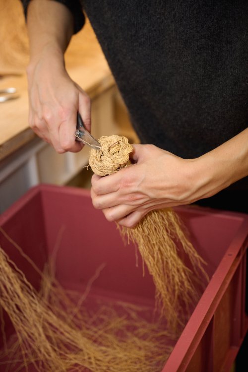 Nahaufnahme von Händen beim präzisen Binden eines handgefertigten Besens aus Naturfasern.