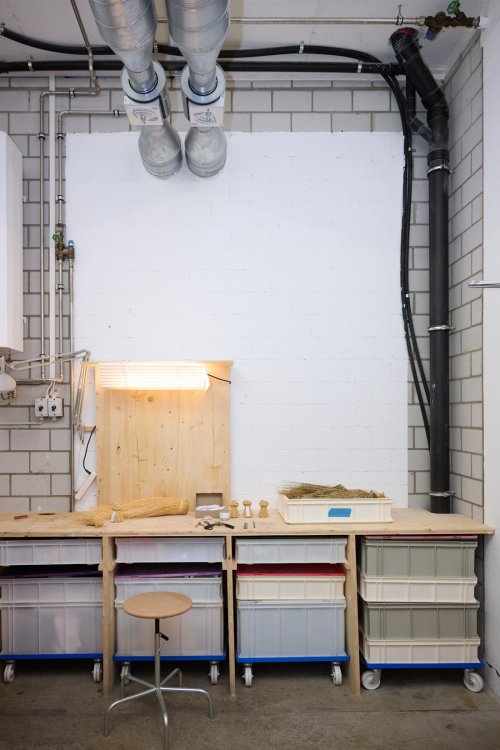 Arbeitsplatz im Atelier von Flavia Brändle mit einer Holzwerkbank, Aufbewahrungsboxen auf Rollen und Naturmaterialien wie Stroh.