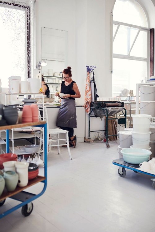 Frau in einer Werkstatt, umgeben von Töpfen und Keramikbehältern