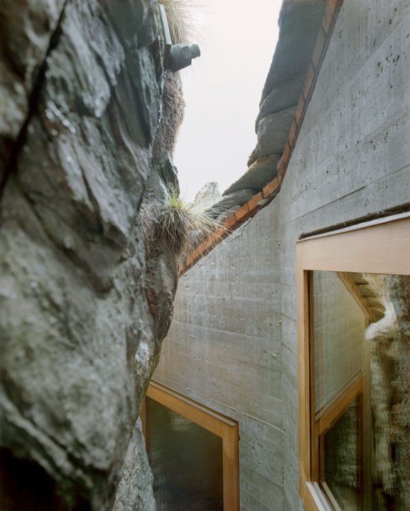Ein Felsen und eine Betonfassade mit zwei Fenstern mit hellem Holzrahmen