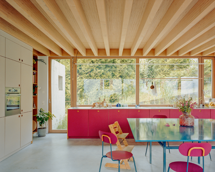 eine rote Küchenzeile vor einem grossen Fenster, davor ein Glastisch mit Sitzgelegenheiten