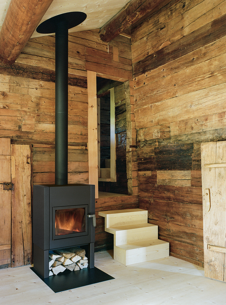 Wohnraum eines alten Holzhauses mit einem Ofen und einer Holztreppe
