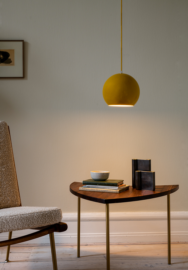 Wohnzimmer mit einem Sessel und braunem dreieckigen Beistelltisch und runder gelber Leuchte.