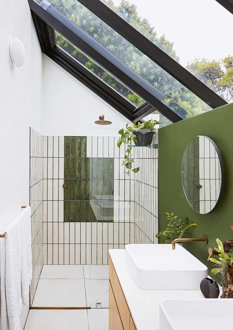Badezimmer mit Schrägdach aus Glas, Dusche und zwei Waschbecken aus weissem Keramik, die Wände rechts sind in einem warmen Moosgrün gestrichen.