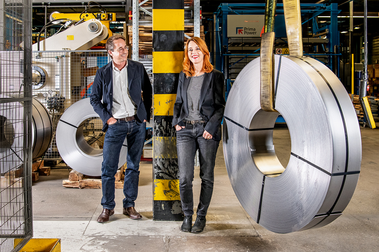 Beni Weber und Sandra Weber Blättler stehen in einer Produktionshalle zwischen runden Metallscheiben.