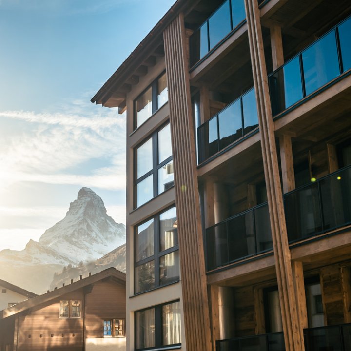 Aussenansicht des Hotels Altiana by La Ginabelle in Zermatt mit einer auffallenden Altholzfassade und Balkonen mit Glasverkleidung.