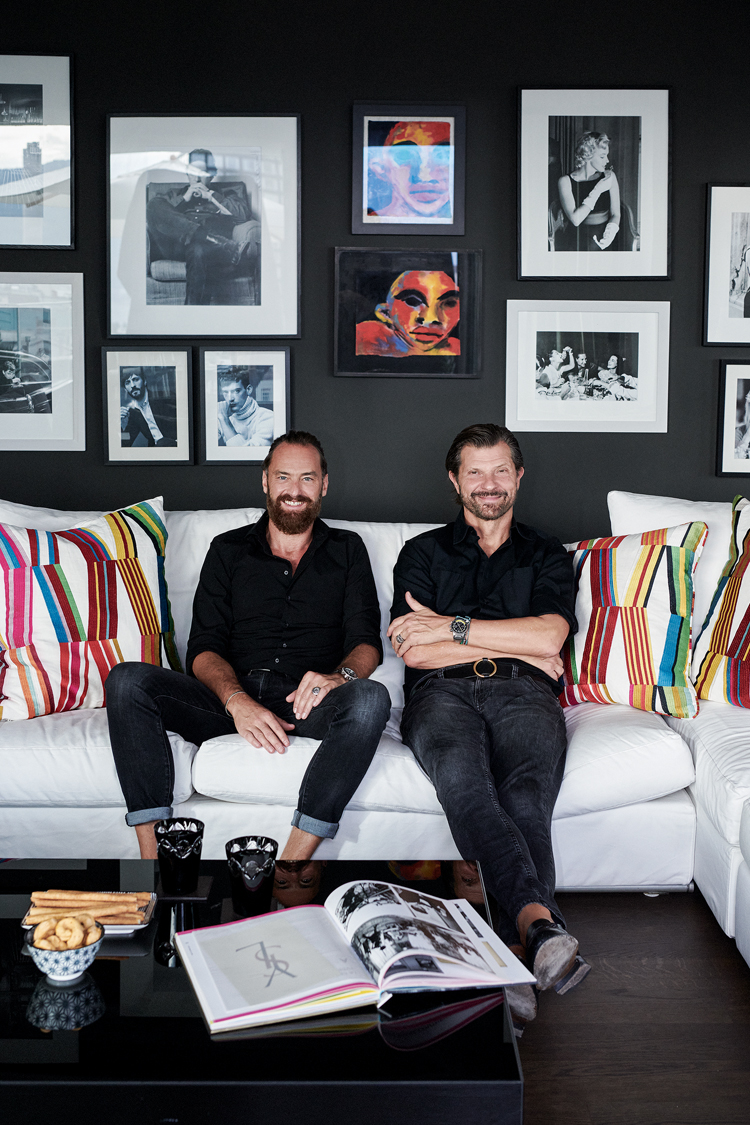 Mario Koch und Erhard Schwendimann sitzen auf einem hellen Sofa vor einer dunklen Wand mit einer üppigen Bildcollage.