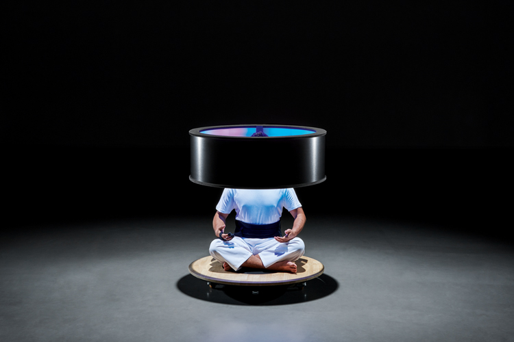 Die Installation «Ming Shan Digital Experience» zeigt eine Person, die sitzt in weissen Kleidern und rund um den Oberkörper und Kopf schwebt ein schwarzer Ring.