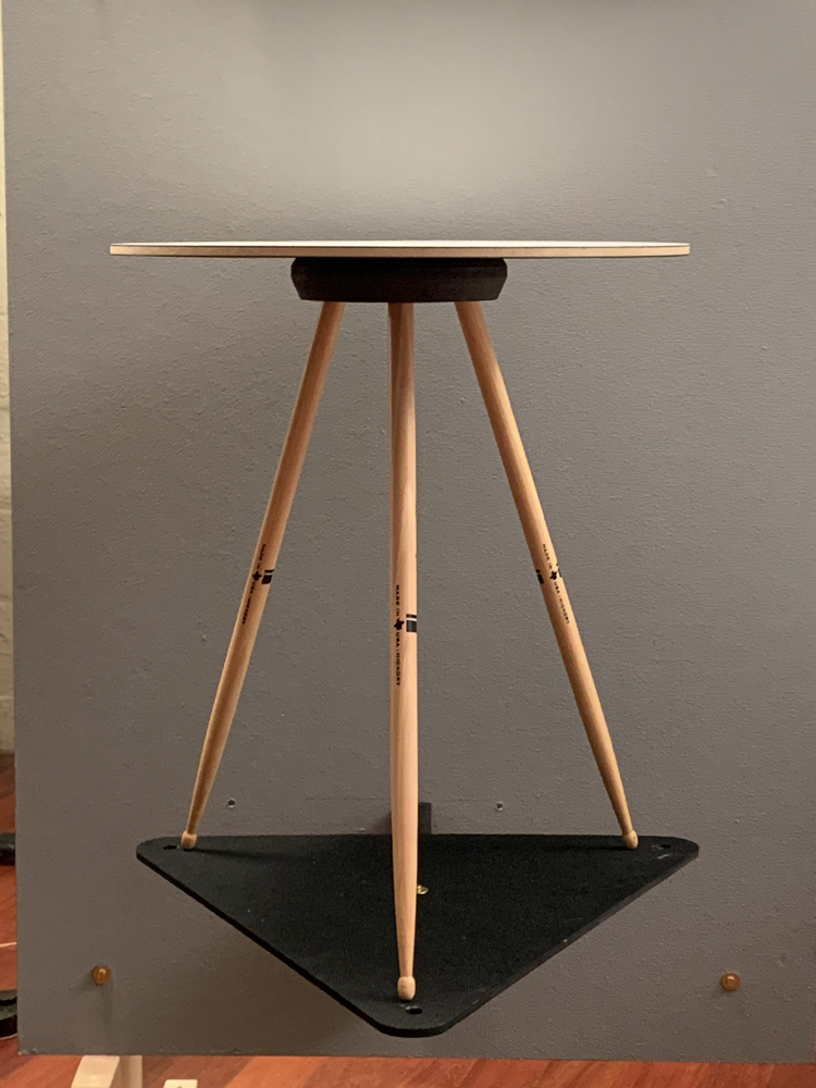 Fotos des Produktes Drum Stick Table von Franz Romero, ein kleiner runder Tisch mit weisser Tischplatte und drei Holzbeinen.
