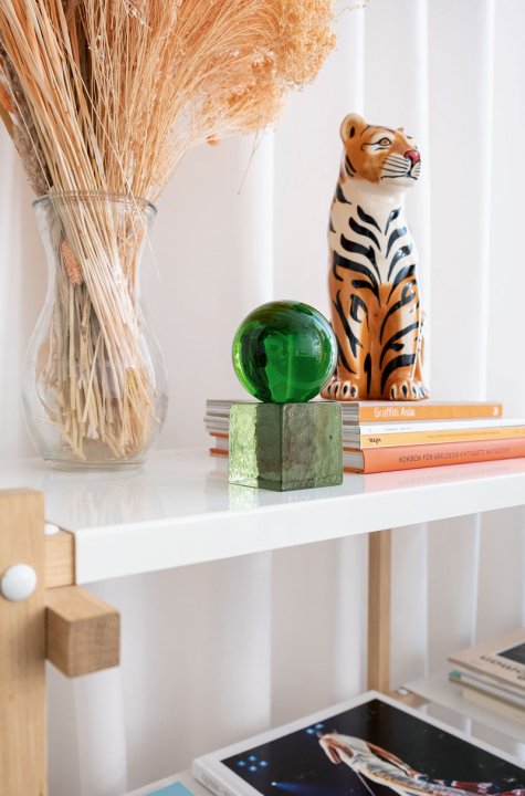 Grüne Glasskulptur steht auf einem weissen Regal neben einem Tiger aus Porzellan.