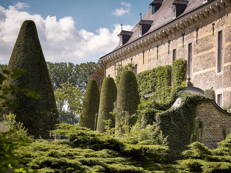 Altes Schlosshausfassade mit grünen Kletterpflanzen und Garten davor.