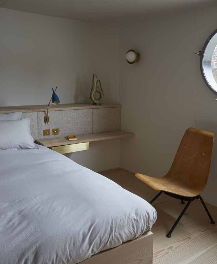 Schlafzimmer mit weisser Bettdecke und einem braunen Sessel auf der rechten Seite, angeschnittenes rundes Fenster.
