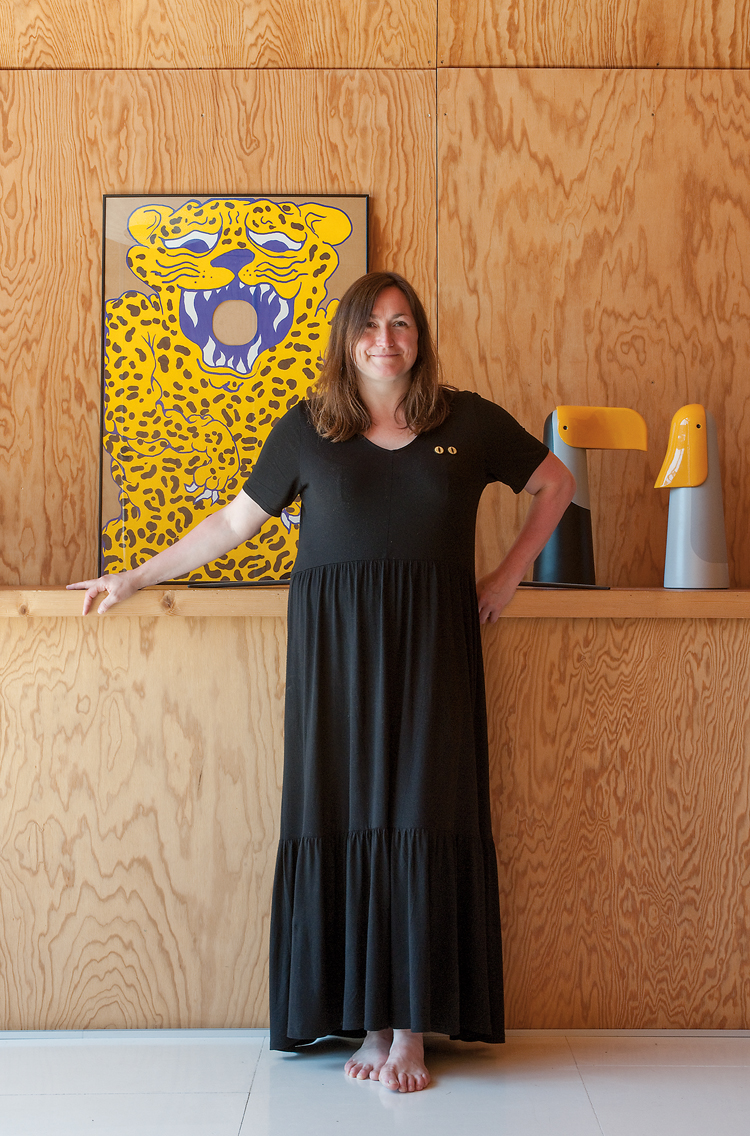 Designerin Ionna Vautrin steht mit einem schwarzen langen Kleid vor einem gelben Bild und Holzwand.