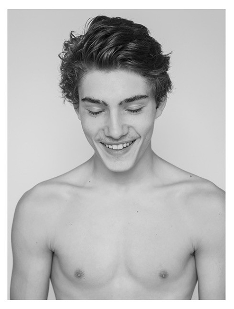 Porträtfotografie eines gebückten jungen Mannes der lächelt und den Blick auf den Boden gerichtet hat in schwarz-weiss.