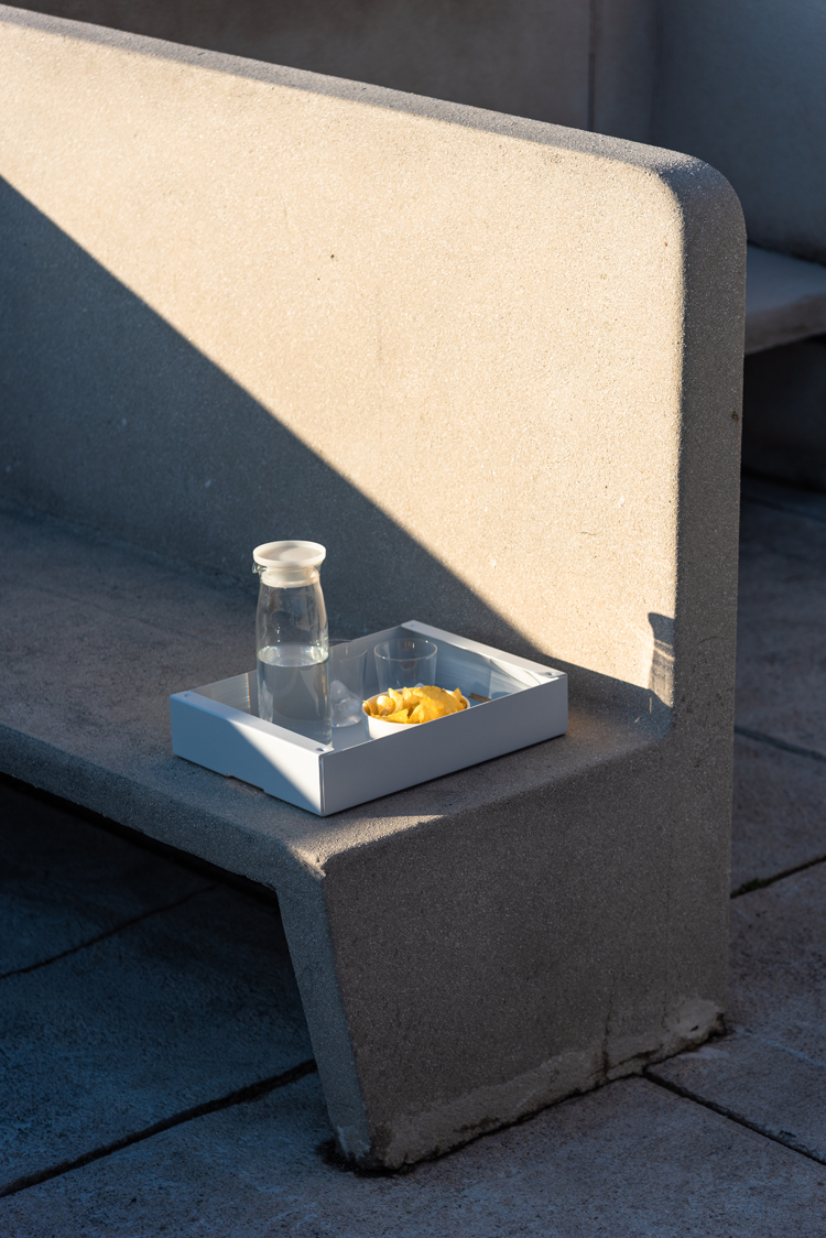 Aufbewarhrungsbox in grau steht auf einer Betonbank und dient als Tablet für eine Karaffe und Gläser.