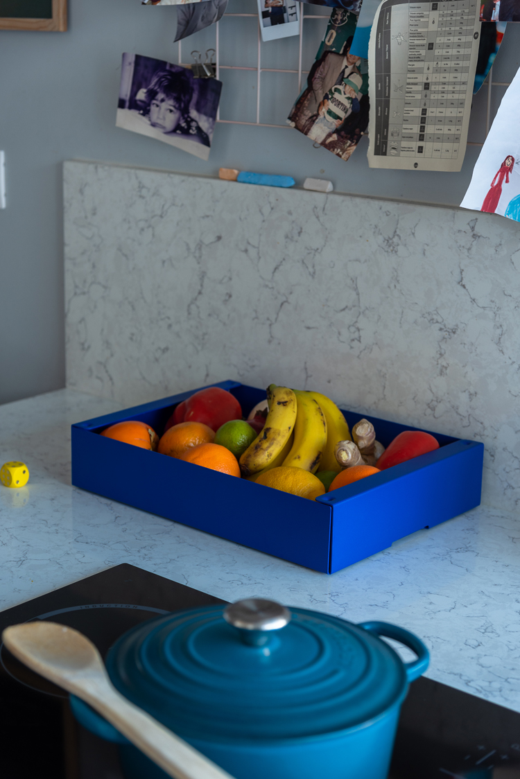 Blaue Aufbewahrungsbox mit diversen Früchten steht neben Herd auf einer weissen Marmorabdeckung.