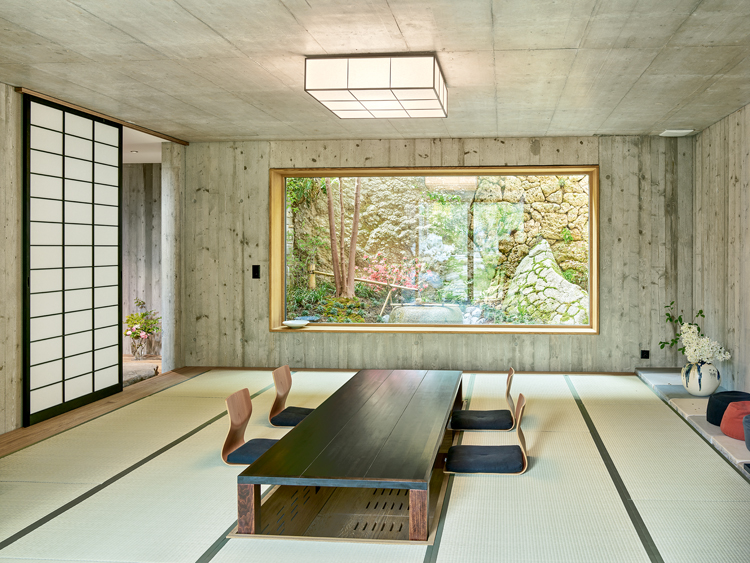 Japanisches Esszimmer mit tiefem Tisch und Hockern vor einem grossen Panoramafenster mit Blick in den Garten.