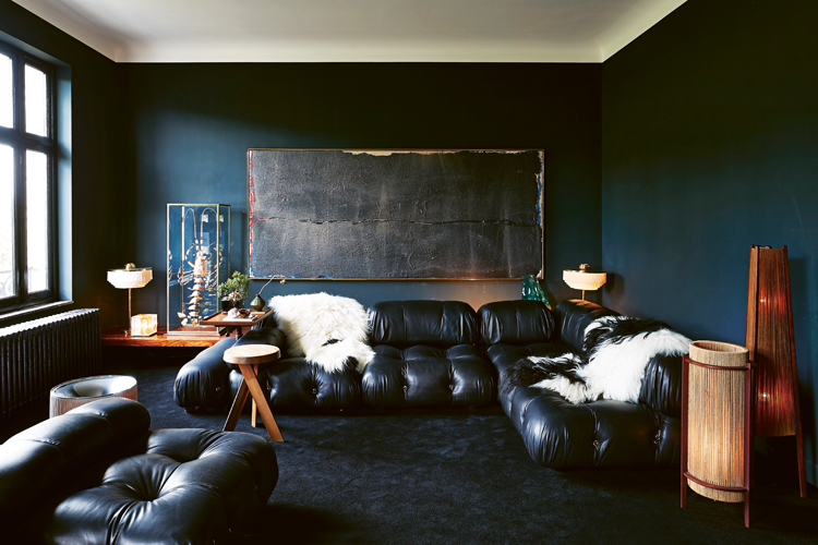 Dunkel gestaltetes Wohnzimmer mit schwarzen, modularen Ledersofas und petrolfarbenen Wänden.