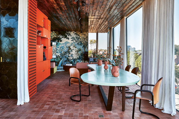 Esszimmer in einem geschlossenen Wintergarten mit oranger Wand und terracottafarbenen Bodenfliessen.