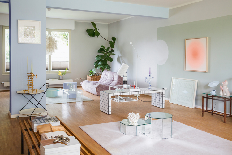 Wohnzimmer mit verschiedenen pastellfarbenen Wänden veilchenfarbenem Sofa und weissem Teppich.