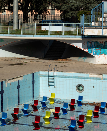 Installation der Neuinterpretation des Zig Zag Stuhls ins Blau, Rot und Gelb in mannigfaltiger Aufführung stehend in einem leeren Schwimmbecken.