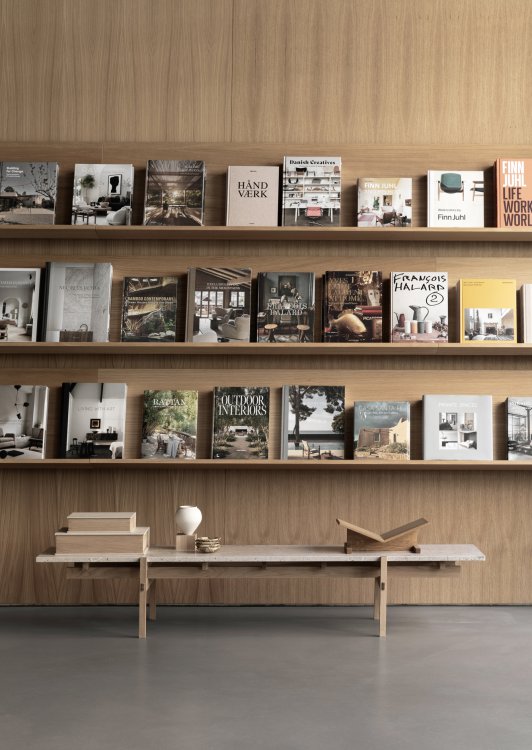 Büchergestell an Holzwand mit ausgestellten Magazincover und einer schlichten Bank.